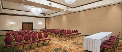 A conference room with rows of red chairs, a white table, and a carpeted floor.