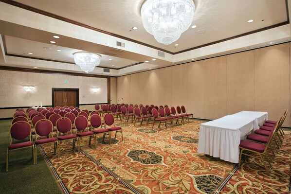 A conference room with rows of red chairs, a white table, and a carpeted floor.