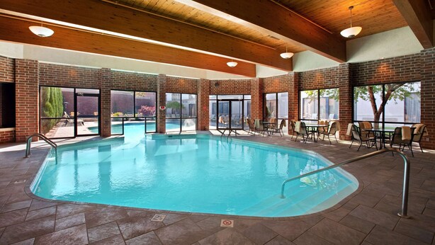 An indoor swimming pool with a brick wall, wooden ceiling beams, and outdoor seating area.