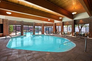 An indoor swimming pool with a brick wall, wooden ceiling beams, and outdoor seating area. - Wyndham Independence (Independence)