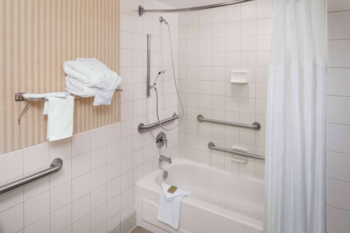 Ein Badezimmer mit Badewanne, Dusche und Handläufen.