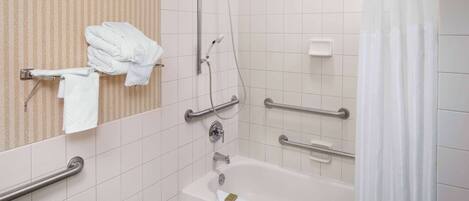 A bathroom with a bathtub, a shower, and handrails.