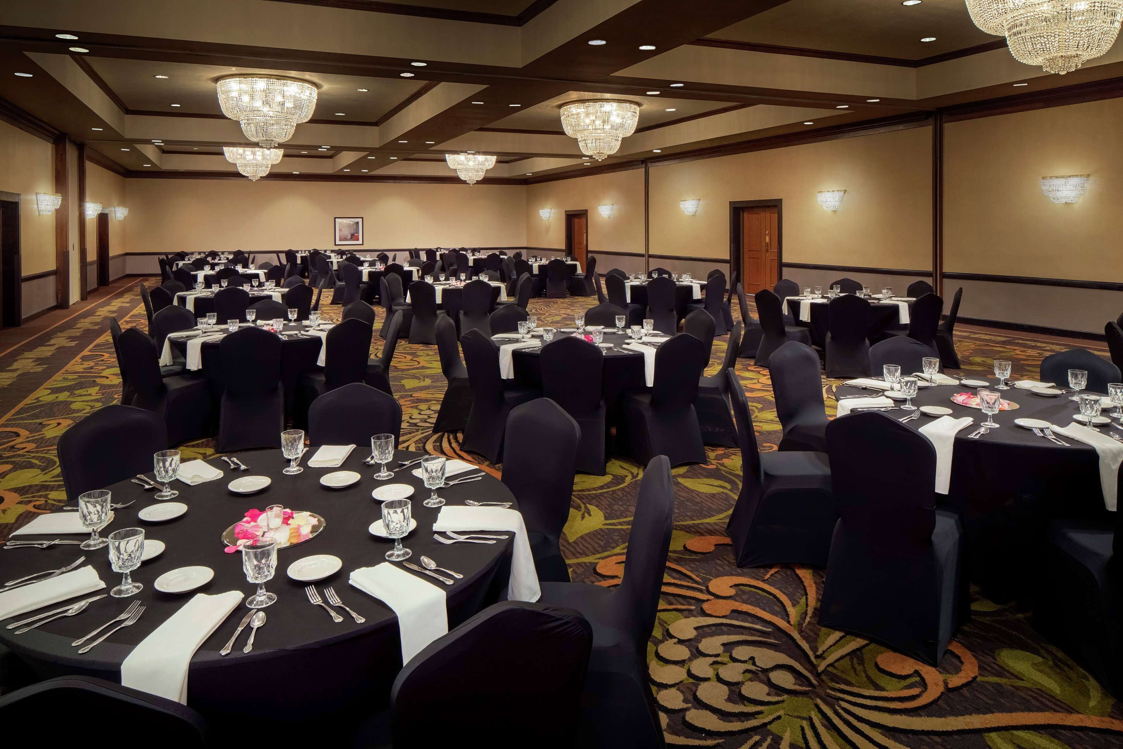 A banquet hall with round tables set for dining, equipped with chairs, tablecloths, and centerpieces.