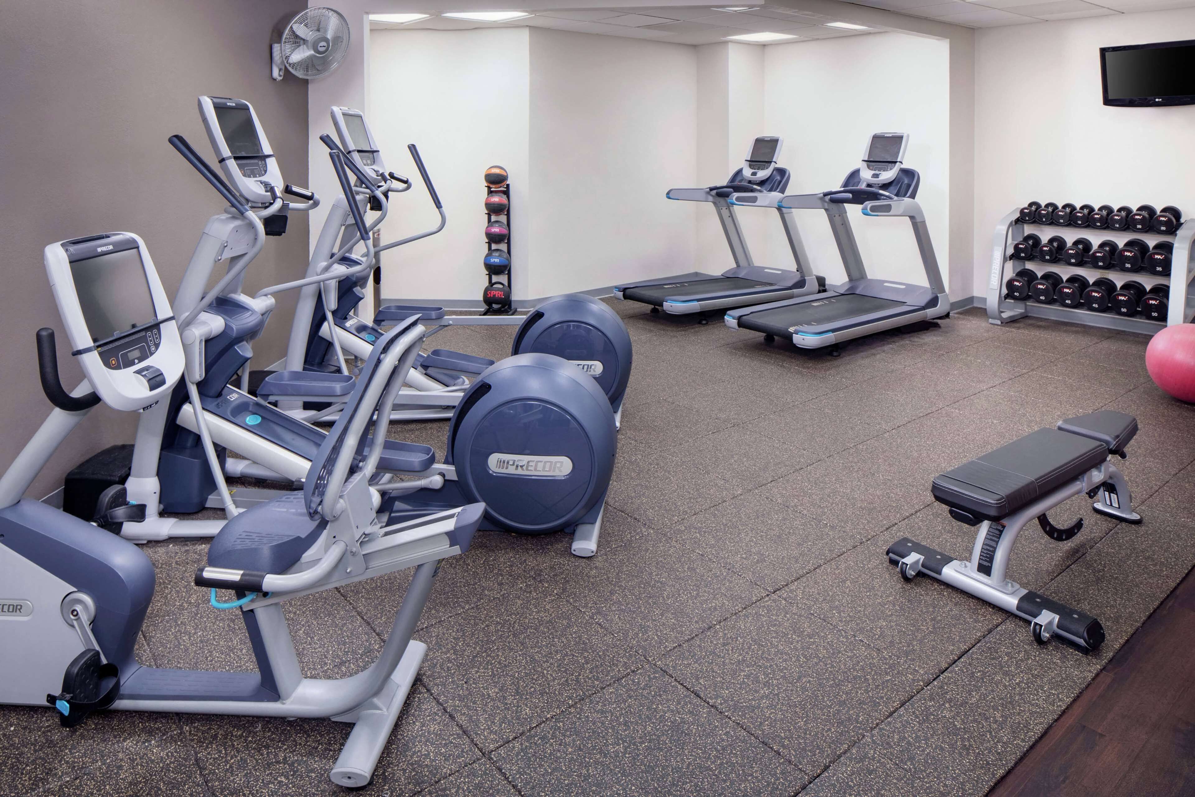 A gym with various exercise equipment including treadmills, elliptical machines, and a bench.