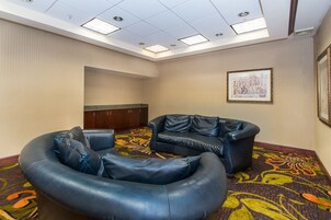 A room with a curved black leather sofa, a wooden cabinet, and a framed picture on the wall.
