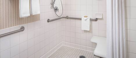 A wheelchair-accessible shower area with grab bars, a white tiled floor, and a white towel rack.