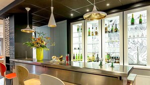 Una zona de bar con mostrador, taburetes, lámparas colgantes y una vitrina de cristal con botellas.