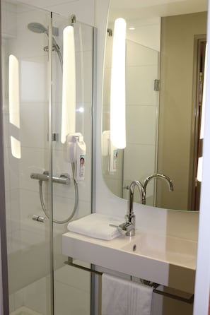 A modern bathroom with a glass-enclosed shower, a white sink, and a large mirror.
