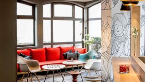 Un interior moderno con un sofá rojo, sillas blancas, una mesa de madera y ventanas amplias.