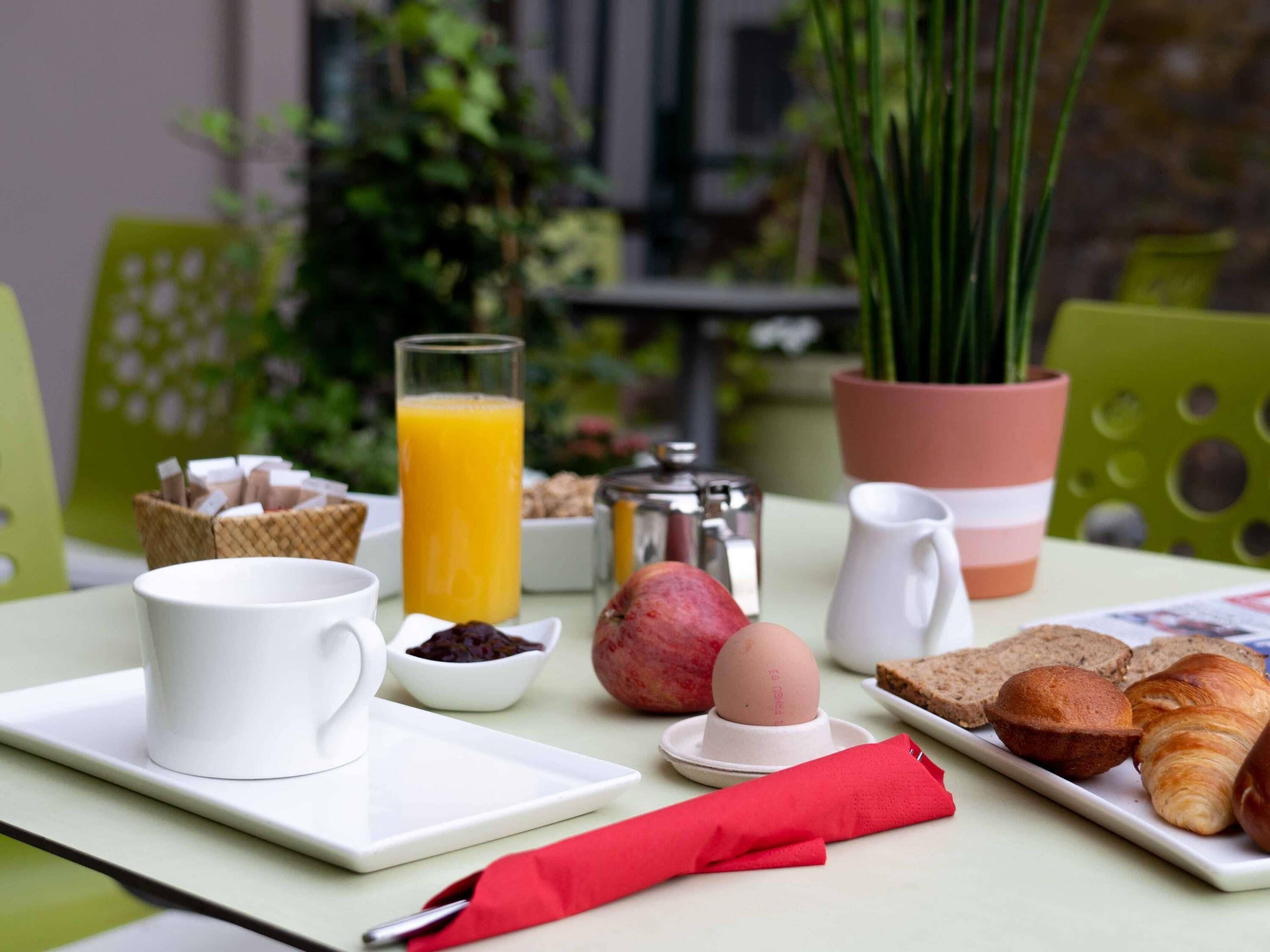Una preparación para el desayuno con una taza de café, jugo, cruasanes y un muffin sobre una mesa.