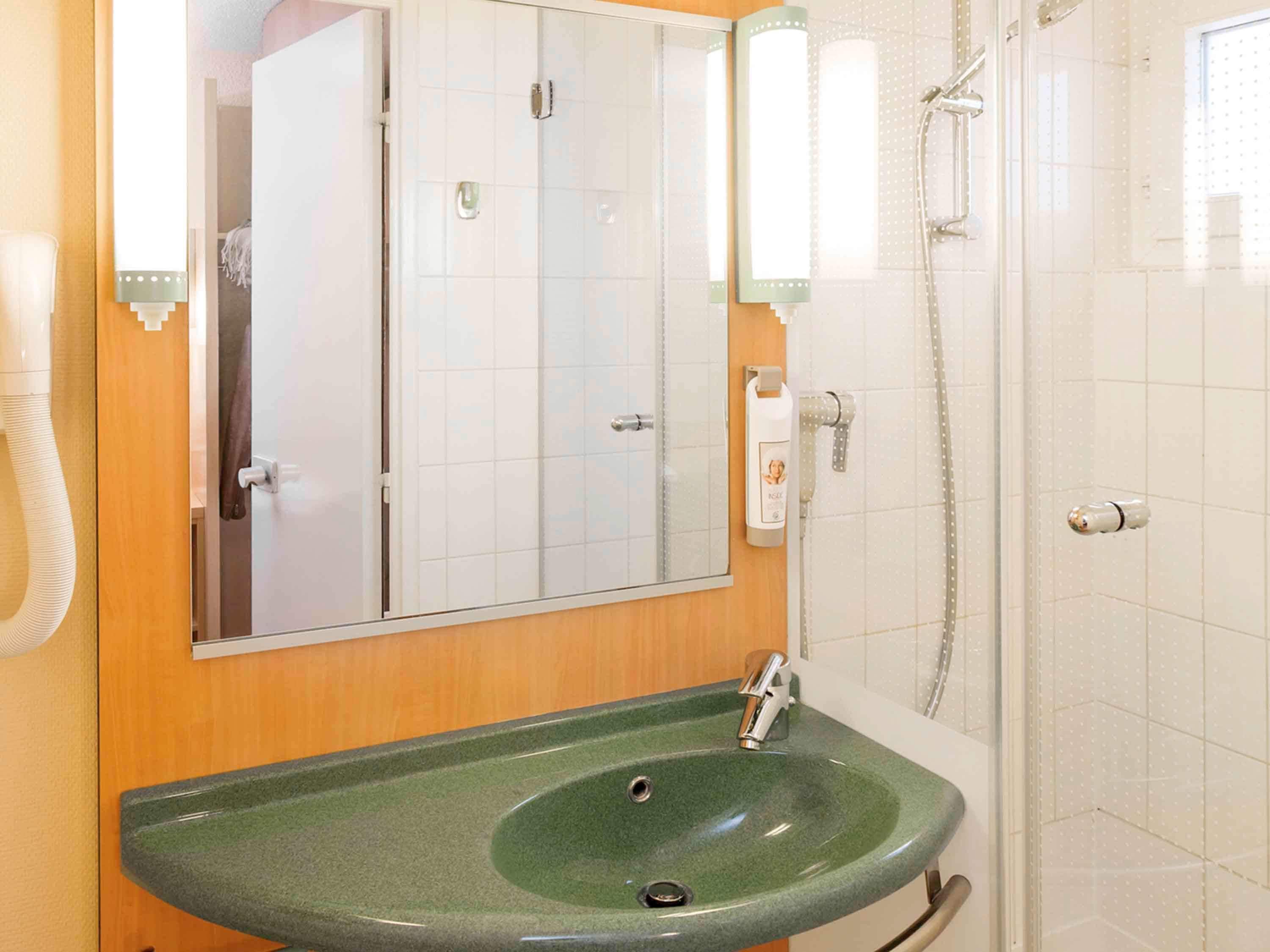 Ein Badezimmer mit einem grünen Waschbecken, einem Spiegel und einer Dusche.