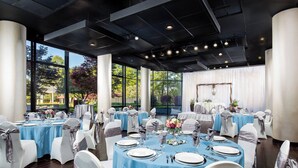 A banquet hall with round tables set for dining, large windows, and a stage with curtains.