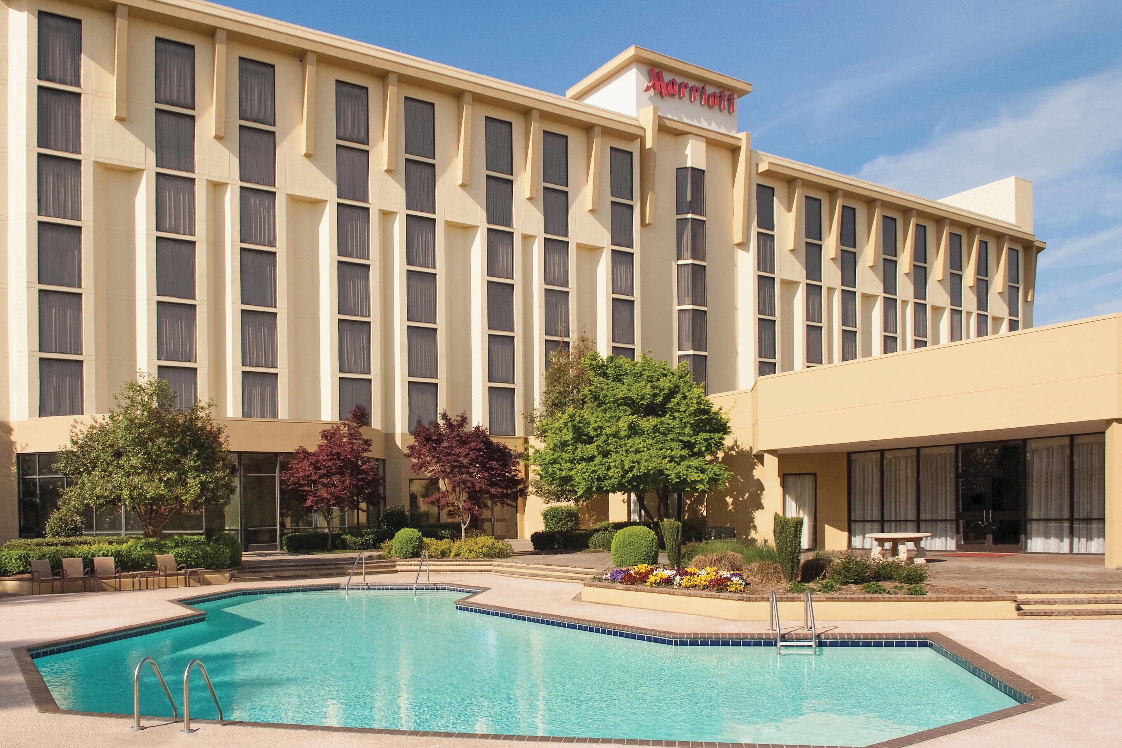 A Marriott hotel with a swimming pool, surrounded by landscaped gardens and a clear sky.