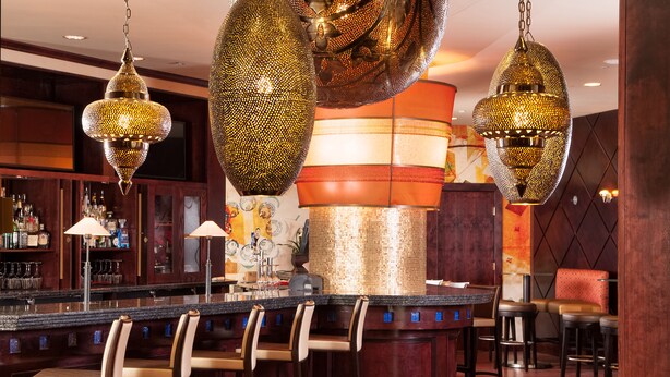 A bar area with multiple hanging decorative lights, a counter with bar stools, and a seating area with chairs.
