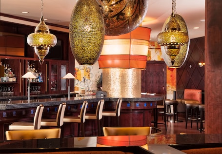 A bar area with multiple hanging decorative lights, a counter with bar stools, and a seating area with chairs.