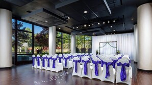 A spacious indoor venue with rows of white chairs adorned with purple sashes, large windows, and a modern ceiling design.