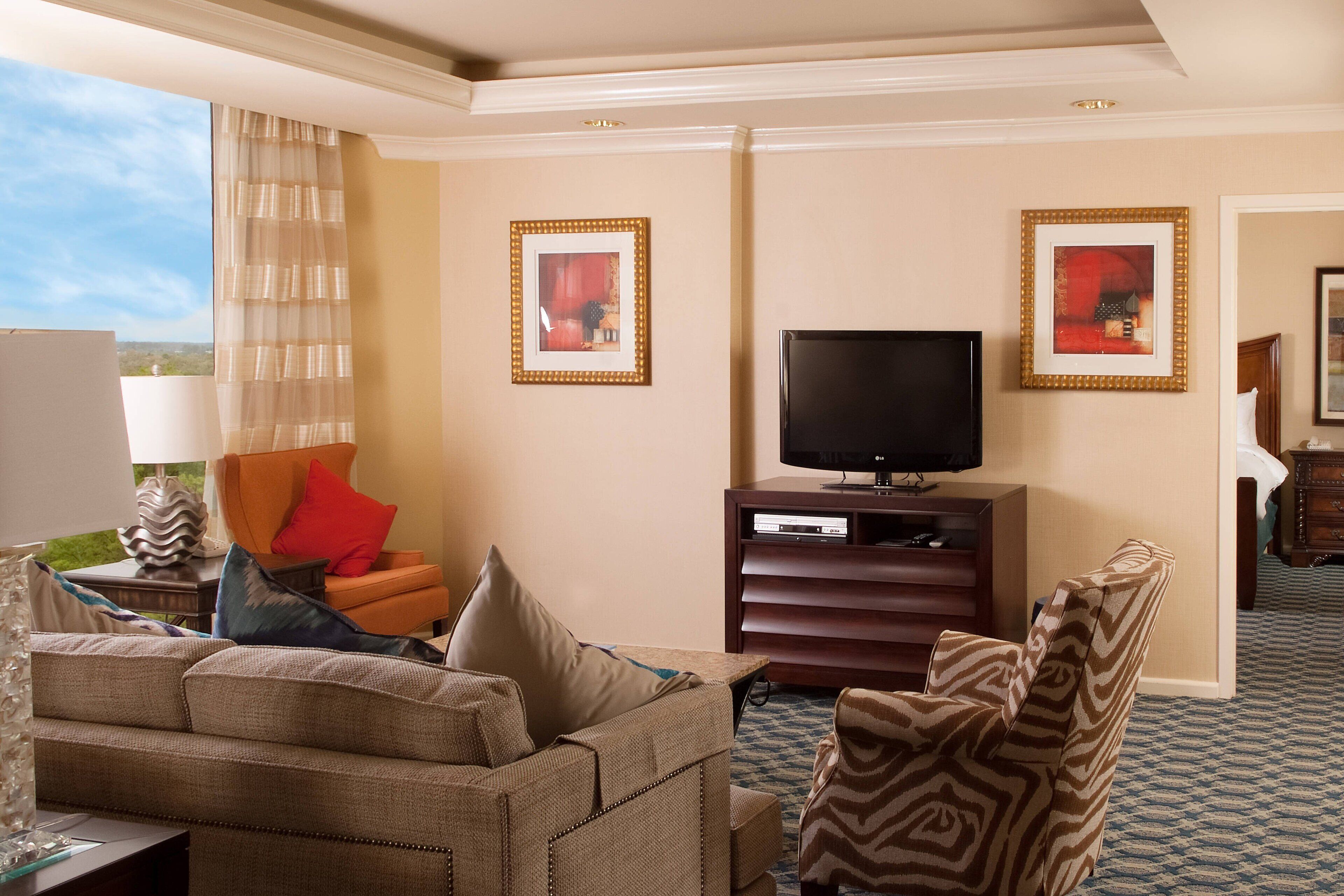 A hotel room with a sofa, armchair, and a television on a wooden stand.