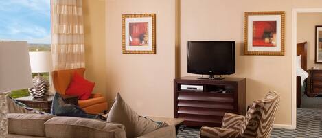 Una habitación de hotel con sofá, sillón y televisión sobre un mueble de madera.