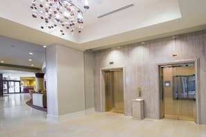 A spacious lobby with a modern chandelier, two elevators, and a reception area. - Greenville Marriott (Greenville)