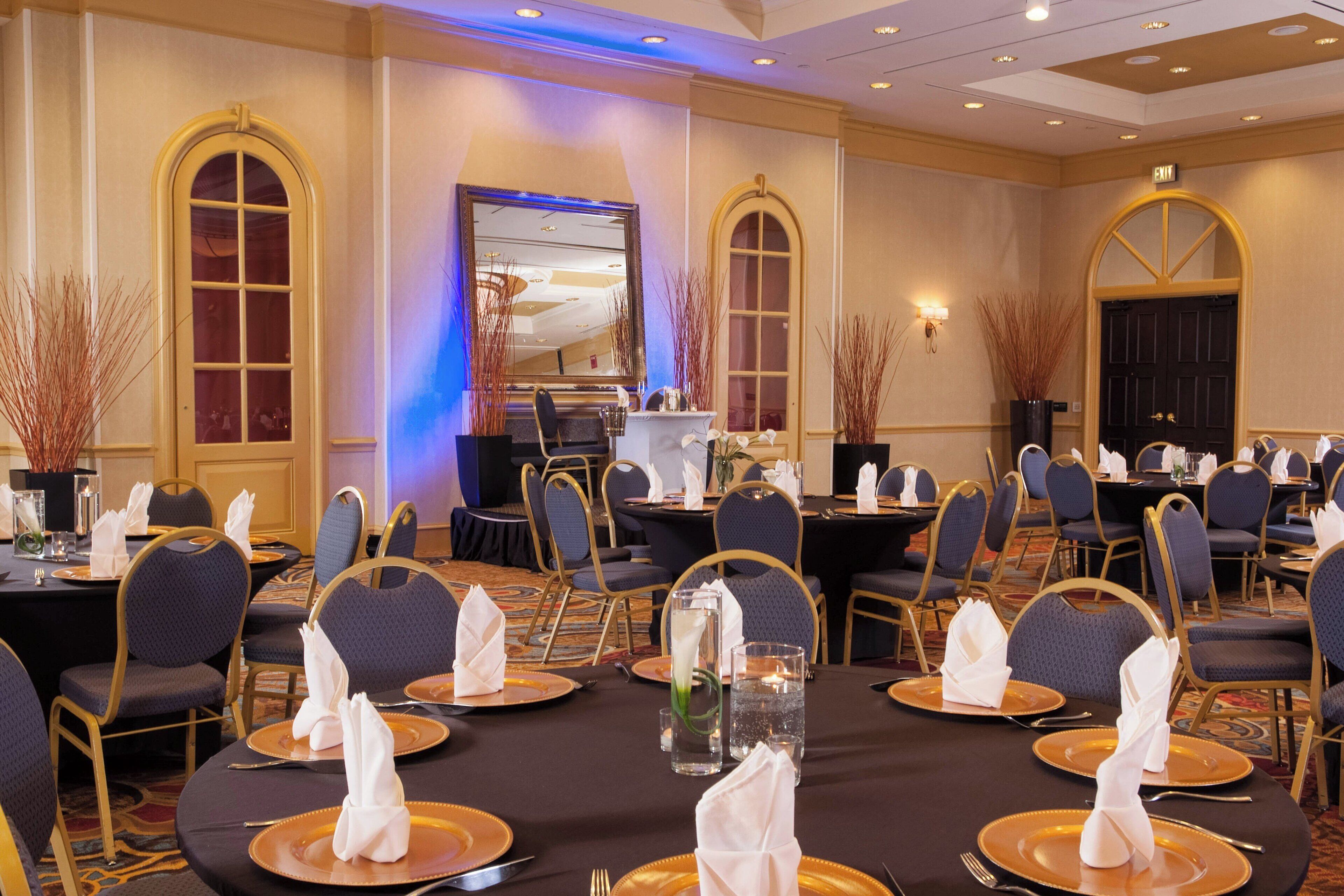 Une salle de banquet avec des tables rondes, des chaises et une scène équipée d’un grand écran.