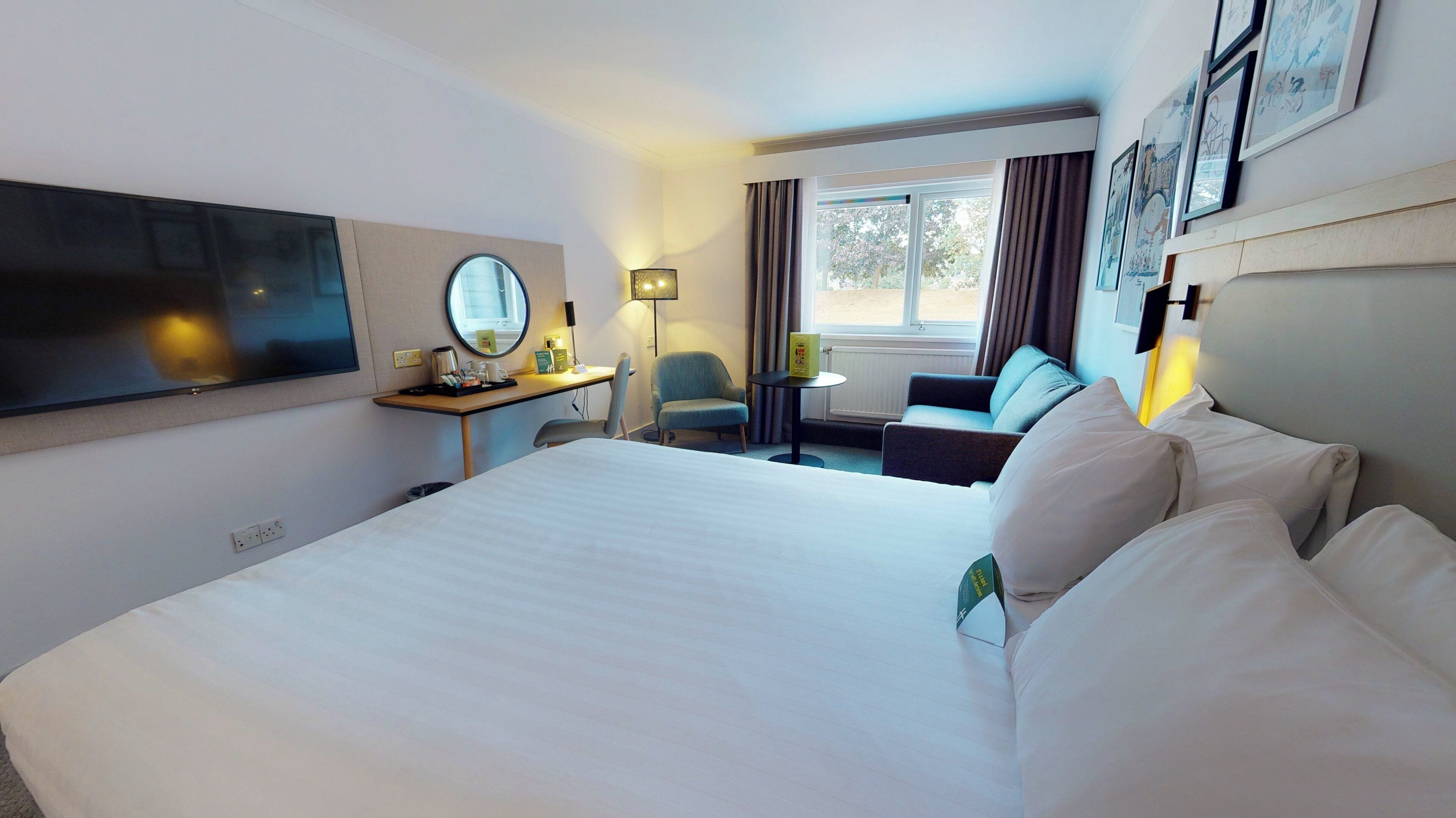 Een hotelkamer met een groot bed, een bureau met een computer, een stoel, een kleine tafel en een aan de muur bevestigde televisie.