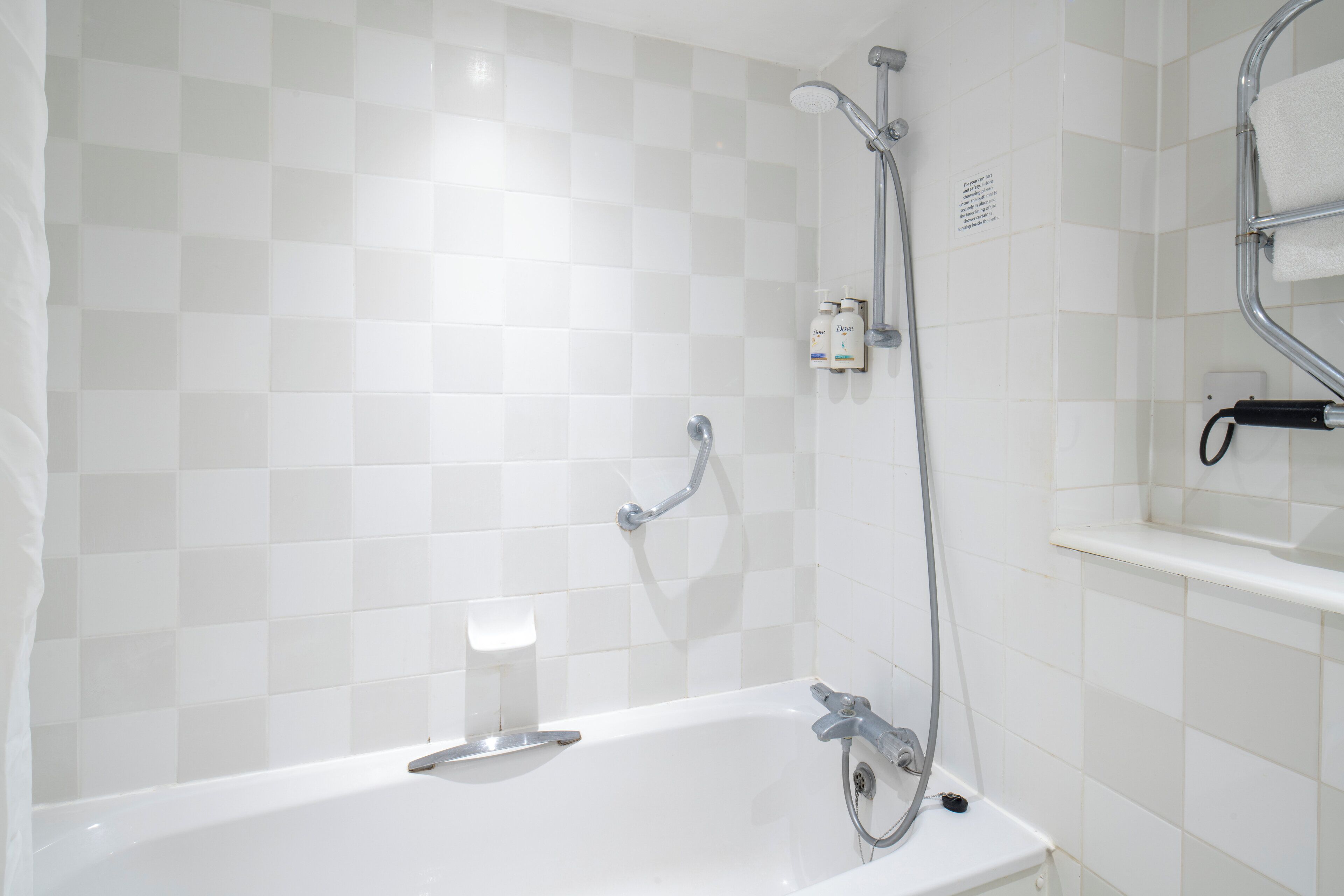 Un baño con una bañera blanca, ducha con cabezal de ducha manual y un perchero con toalla.