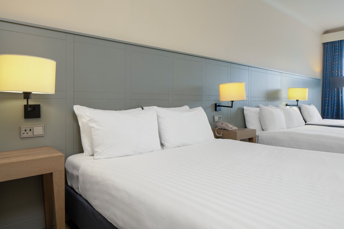 A hotel room with two beds, a bedside table, a lamp, and a phone on the nightstand.