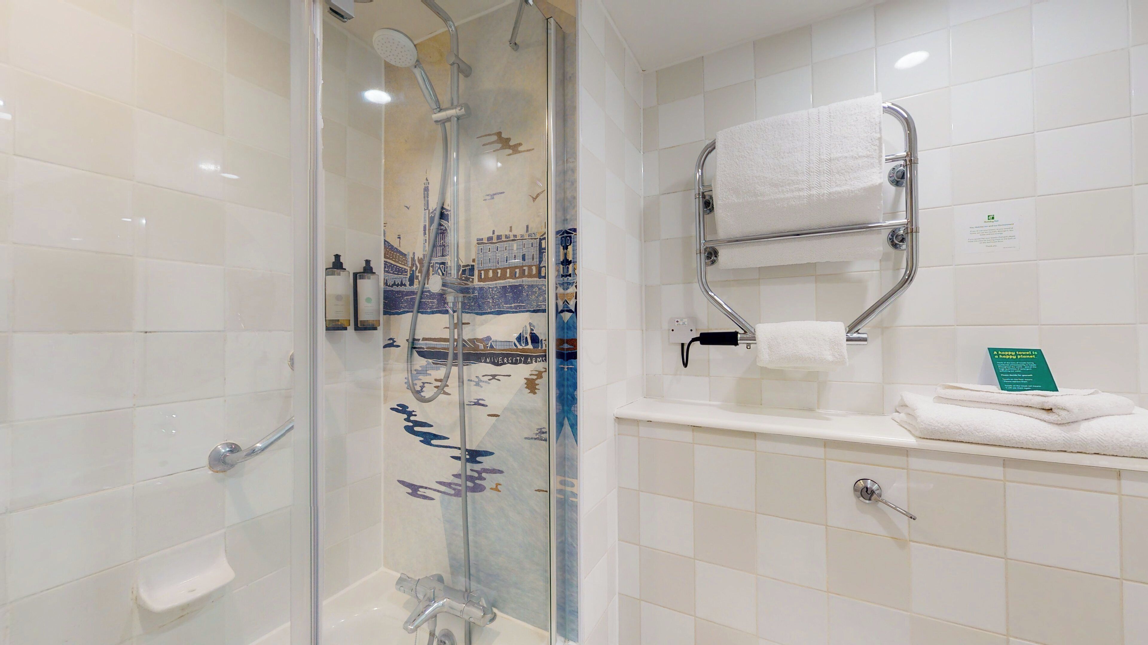 A shower with a glass door, a towel rack with a folded towel, and a sign on the wall.