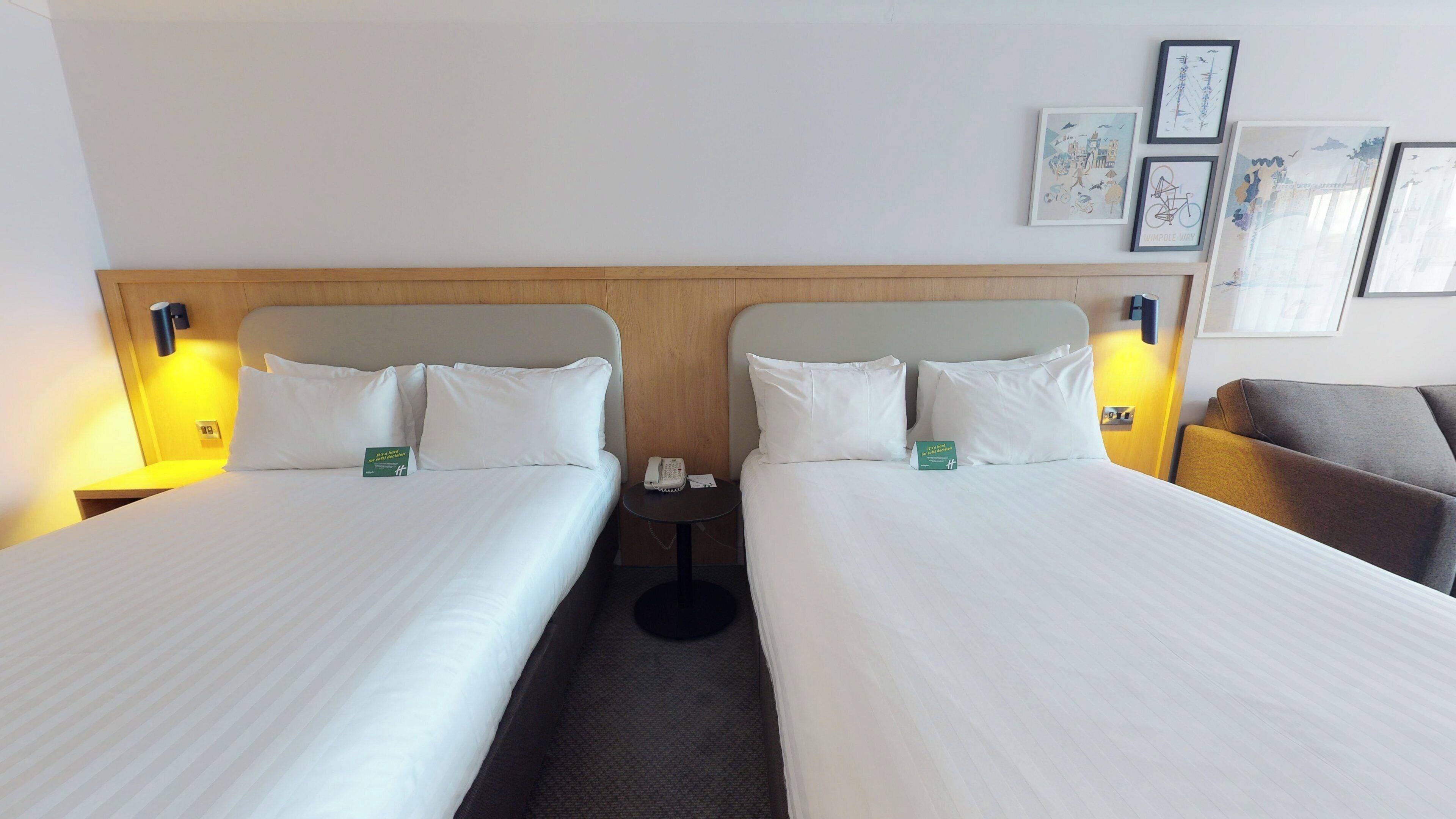 A hotel room with two beds, a bedside table with a phone, and a small round table.