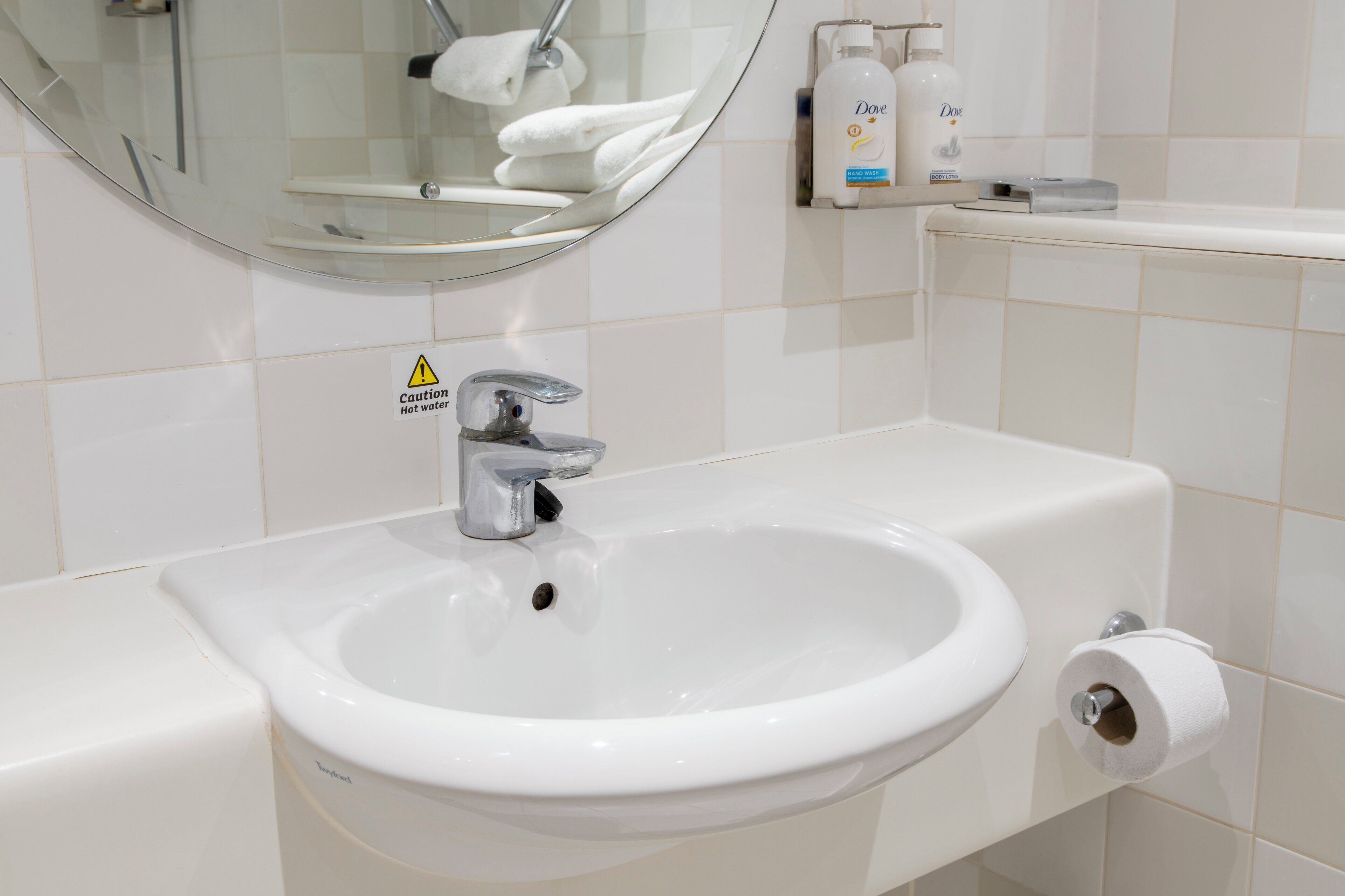 A bathroom with a white sink, a mirror, a caution sign, and toiletries.
