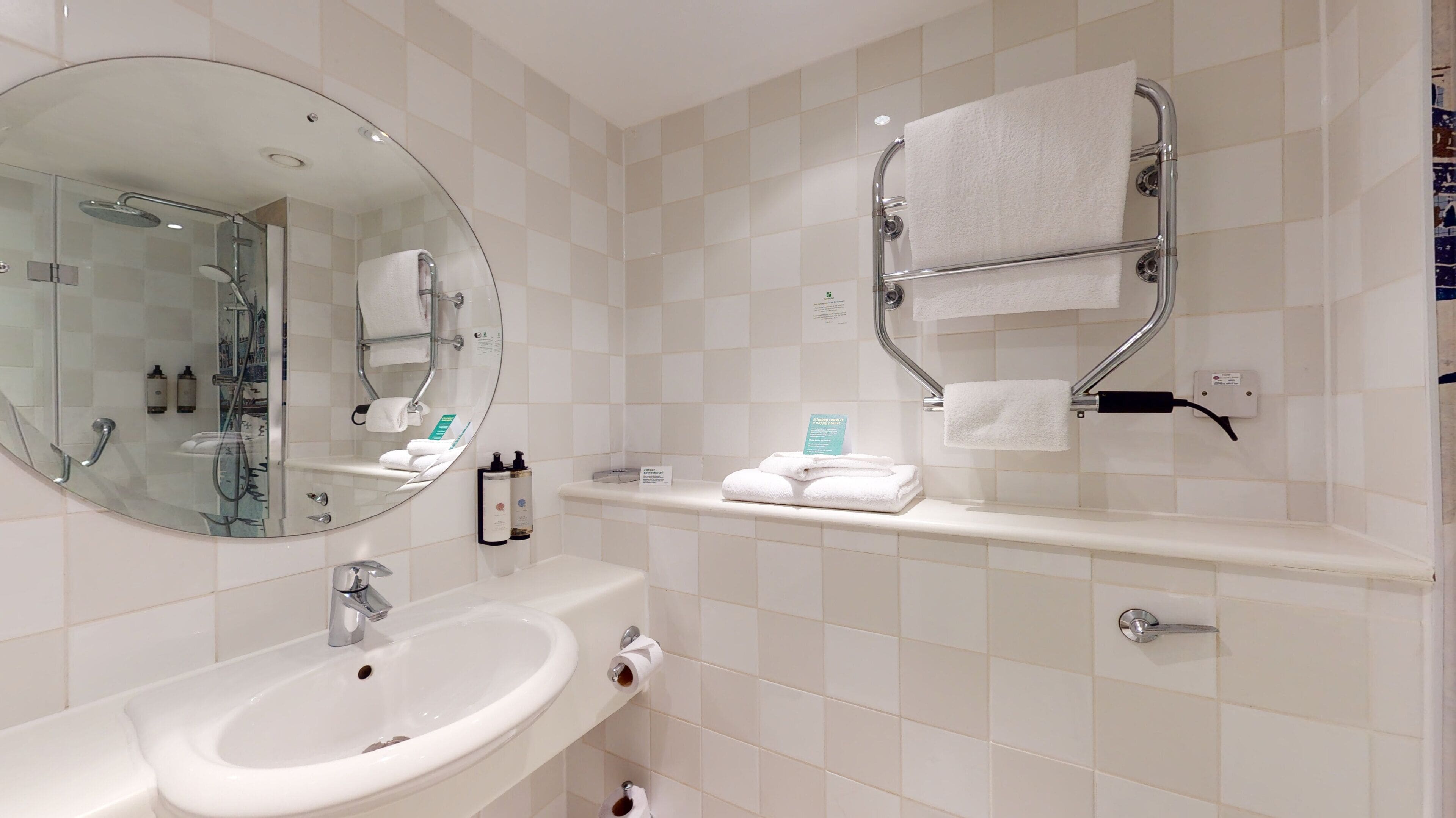 Une salle de bain avec un miroir rond, un lavabo, un porte-serviettes et un espace douche.