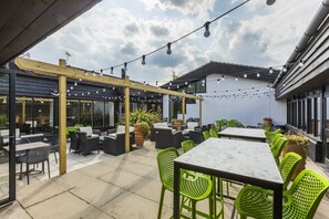 An outdoor patio with tables and chairs, string lights, and potted plants.