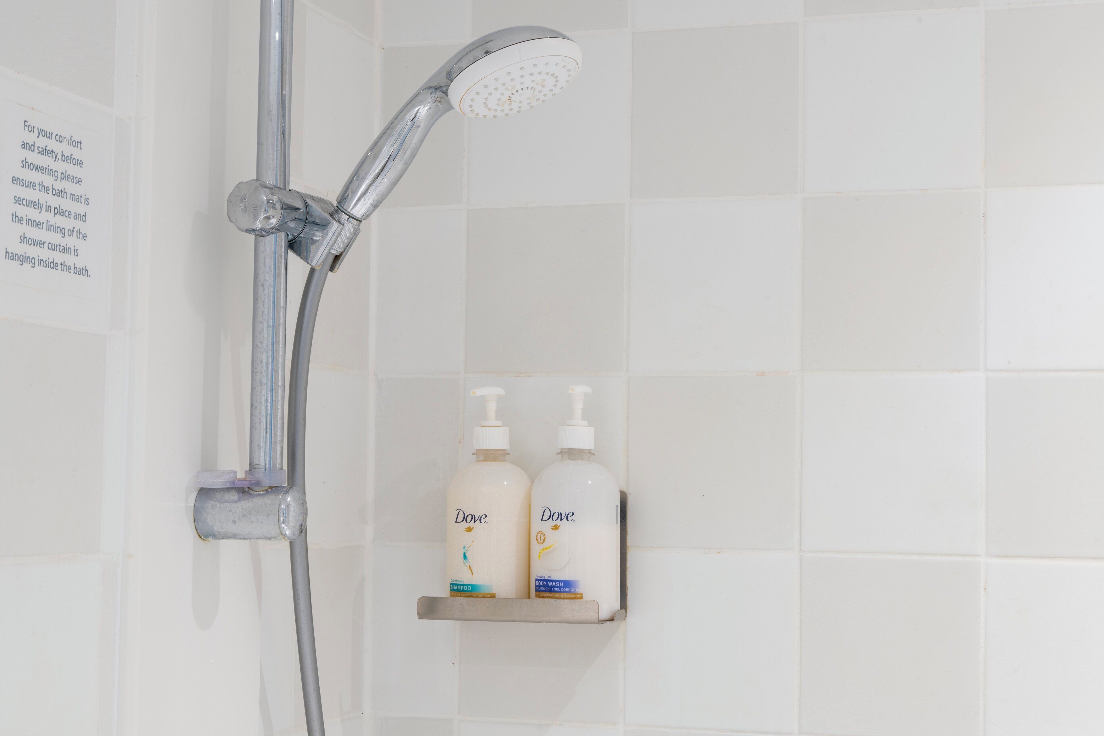 A shower with a handheld showerhead and a wall-mounted control valve. There are two Dove body wash bottles on a shelf below the shower.