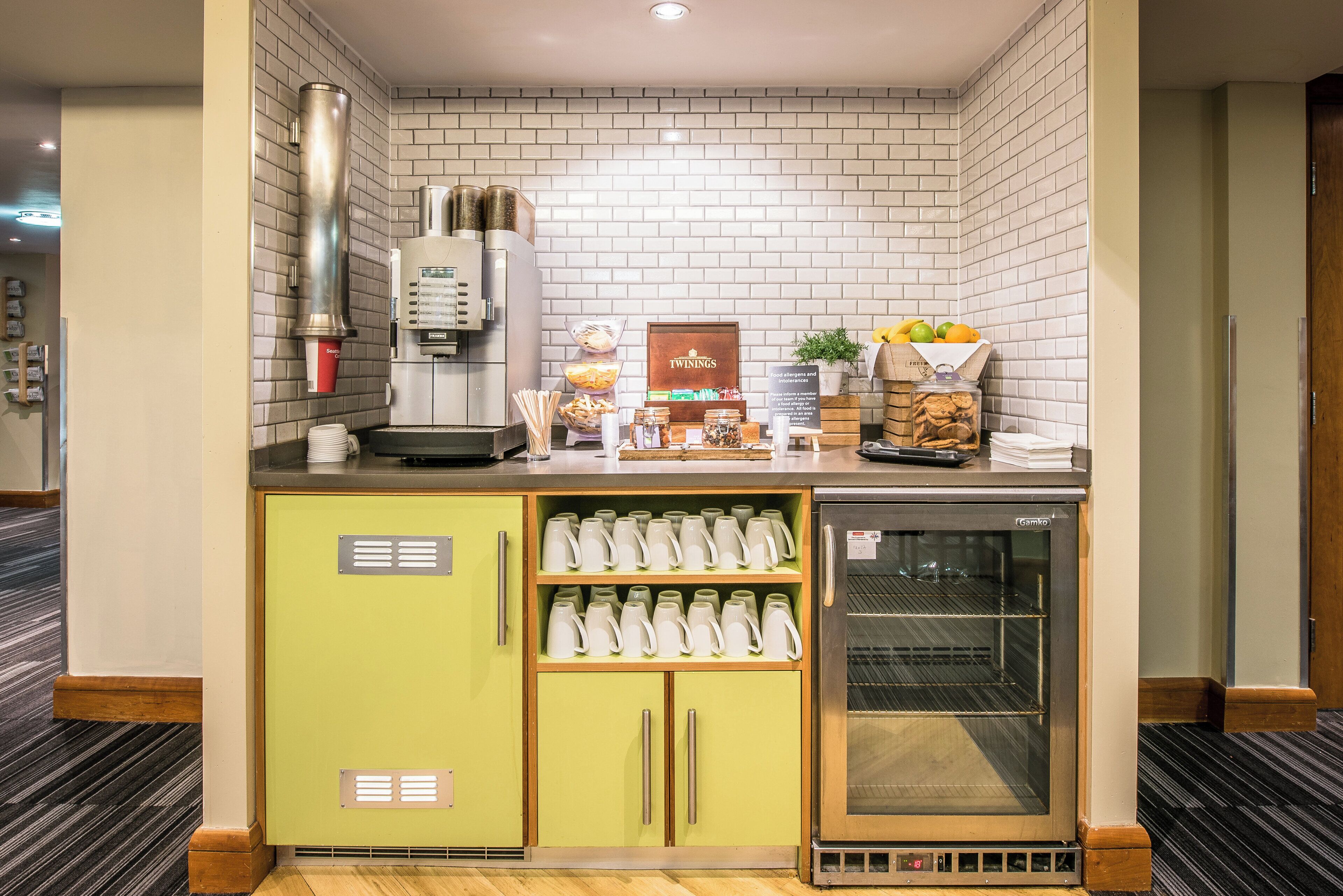 Eine Küchenzeile mit Kaffeemaschine, Kühlschrank und einer Ablage für Tassen und Snacks.