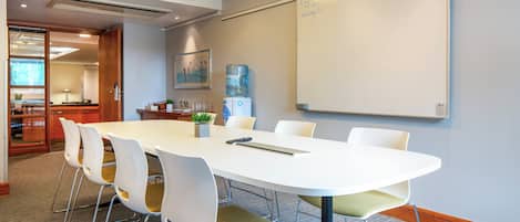 A conference room with a white table, white chairs, a water cooler, and a whiteboard.