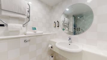 Un baño moderno con pared de azulejos blancos, un espejo redondo, un lavamanos y un perchero para toallas.