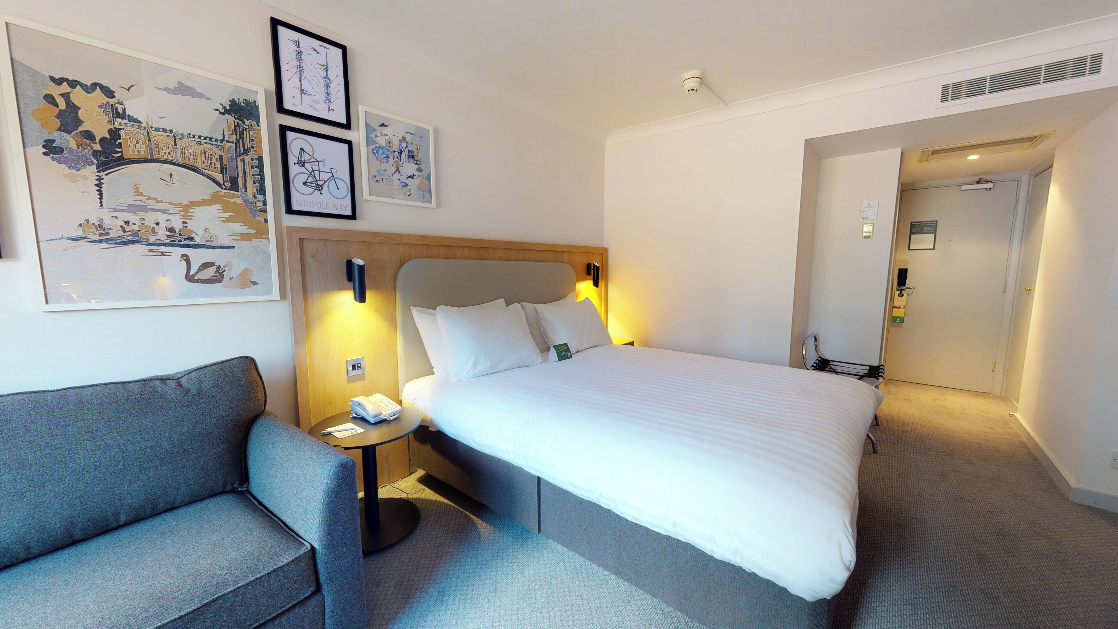 A hotel room with a bed, a nightstand, a chair, and wall art.