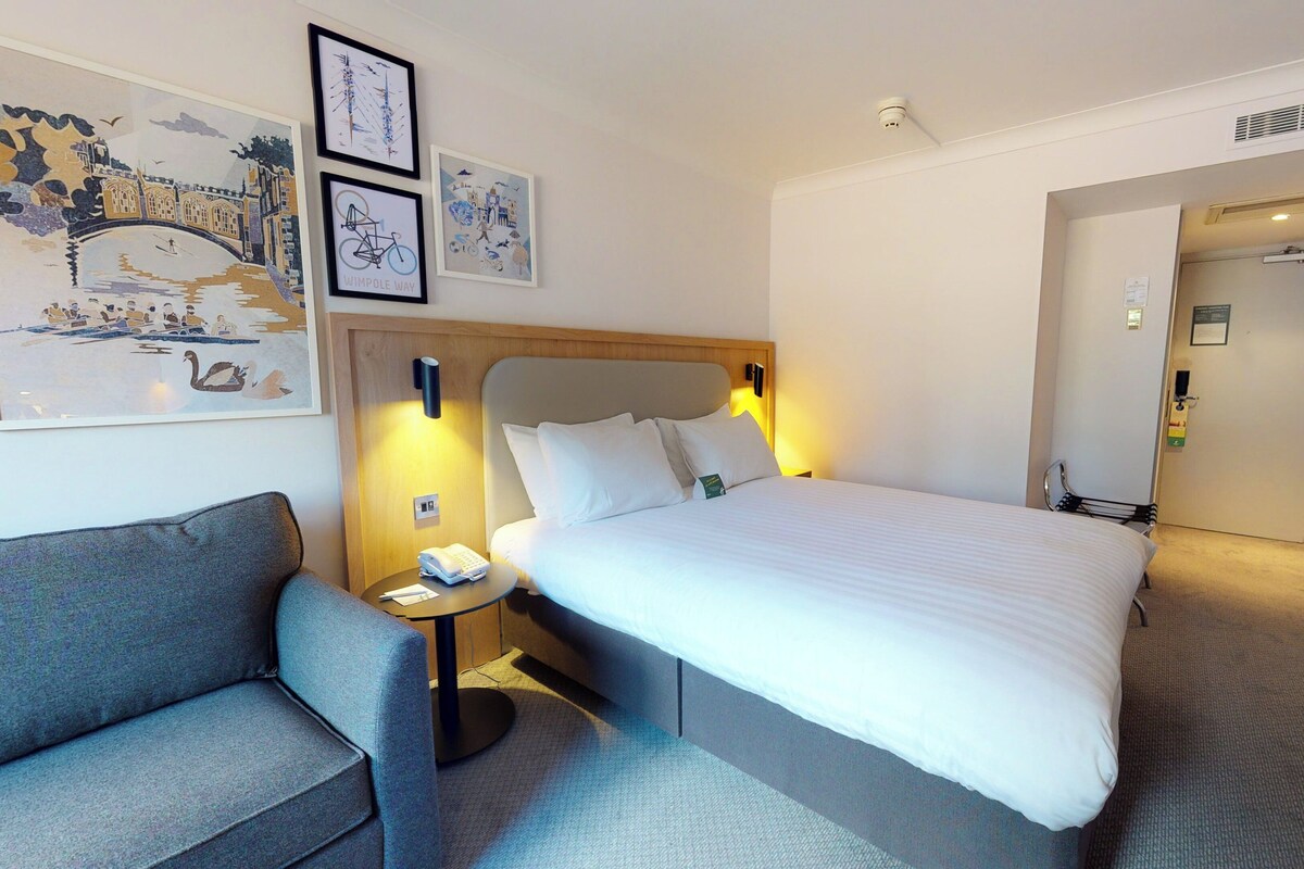 A hotel room with a bed, a nightstand, a chair, and wall art.