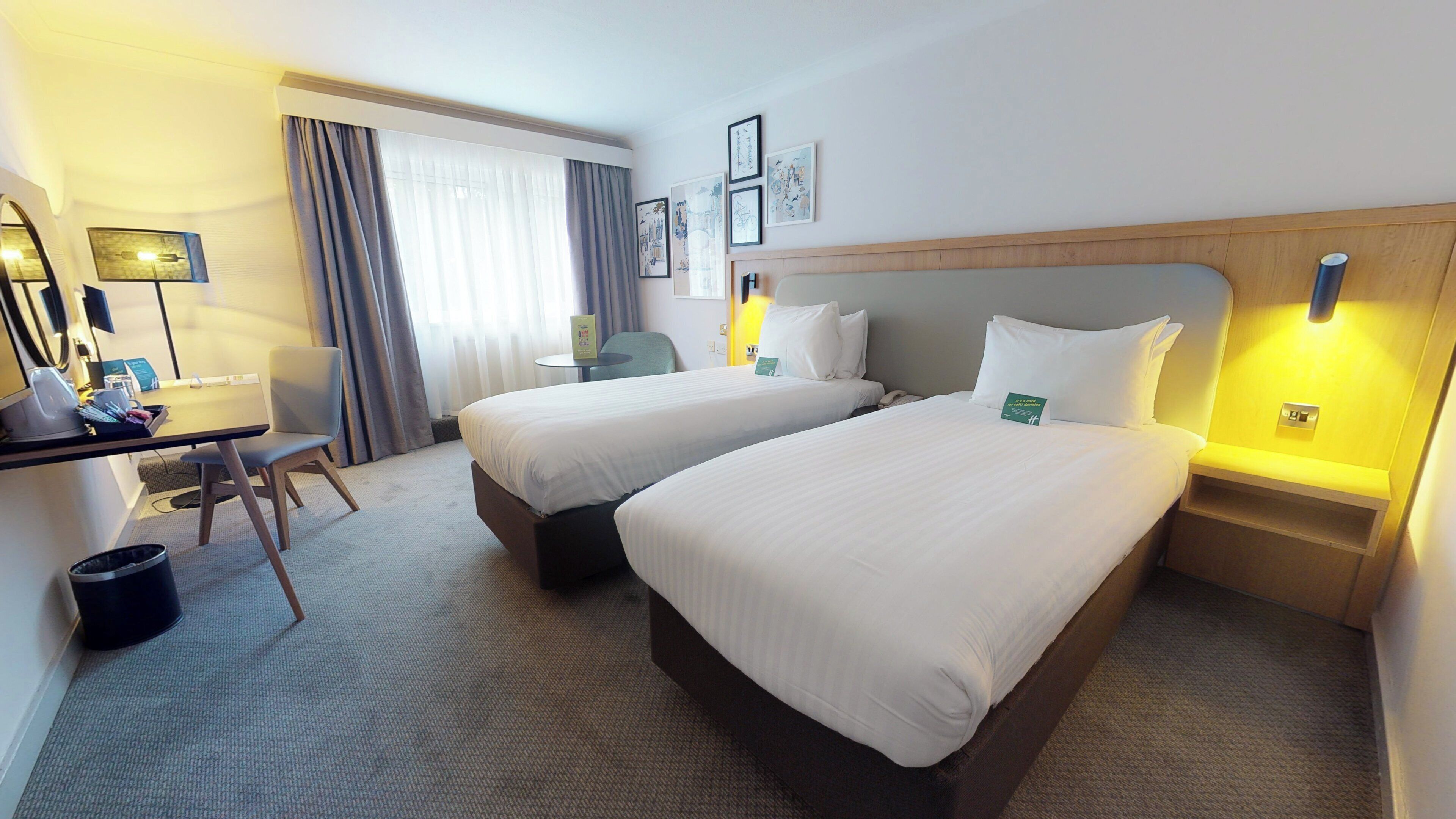 A hotel room with two beds, a desk, a chair, and a small table.