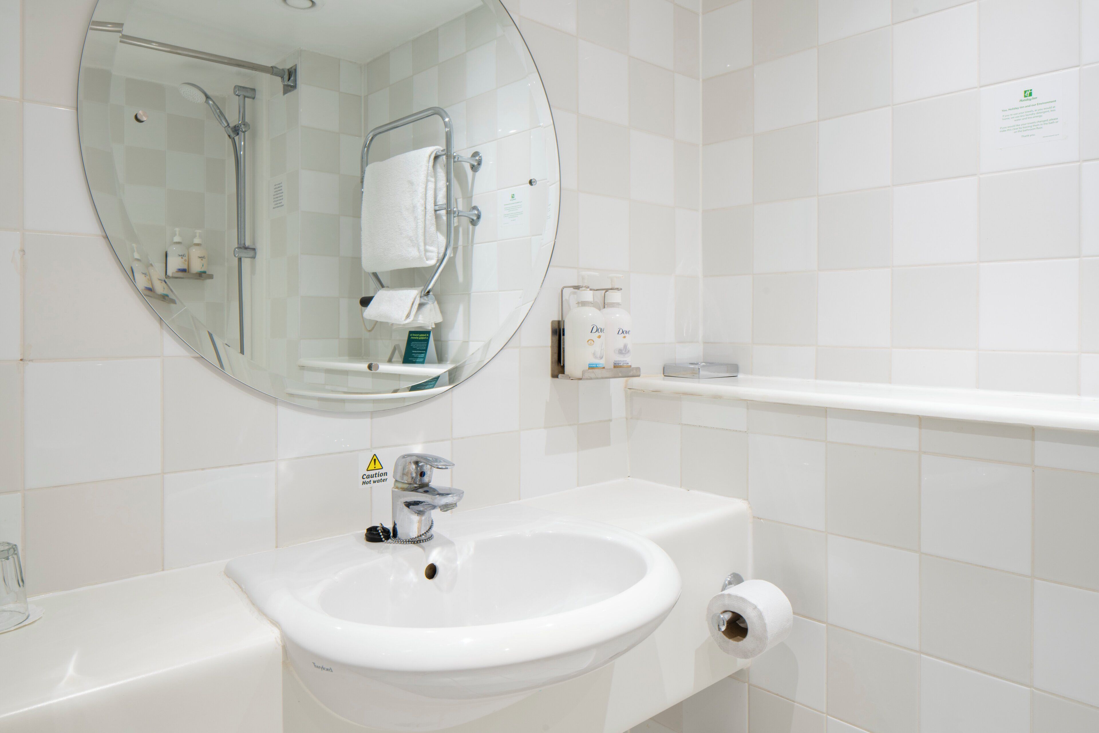 A bathroom with a round mirror, a sink, a shower, and a toilet.