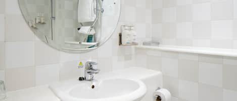 A bathroom with a round mirror, a sink, a shower, and a toilet.