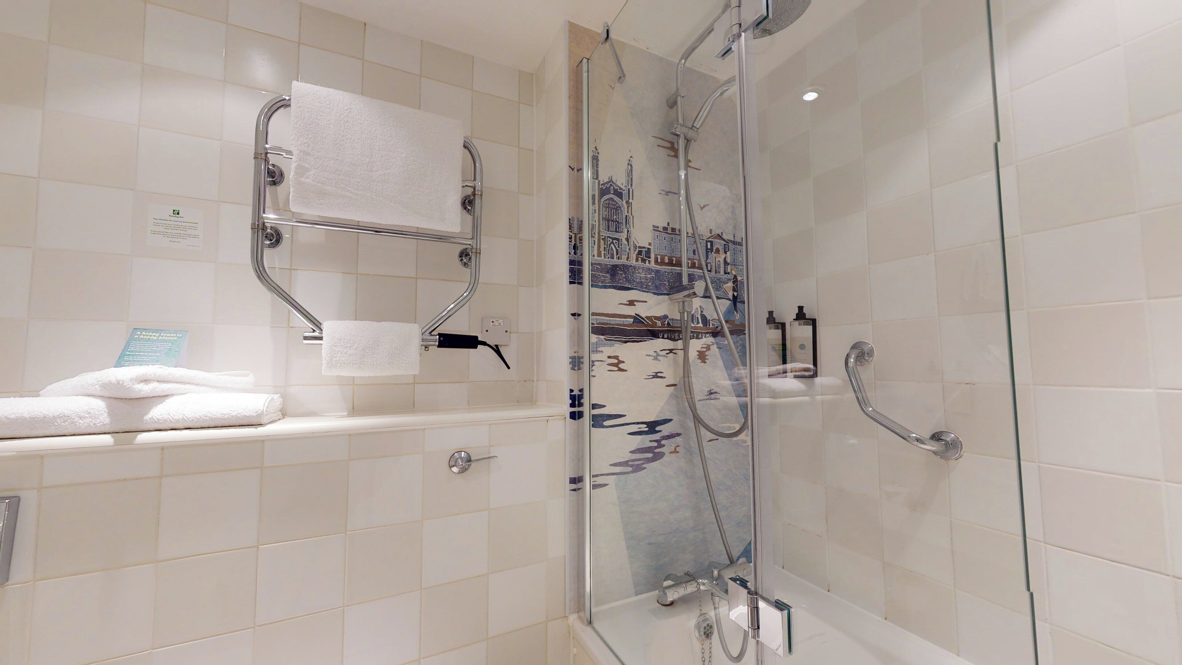 Un baño moderno con ducha acristalada, bañera con puerta de cristal y un perchero con dos toallas.