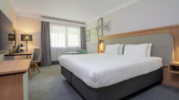 Una camera d'albergo con un letto grande, una scrivania, una sedia e una finestra con tende.