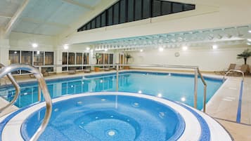 Una piscina interior con jacuzzi, sillones de descanso y un techo con tragaluces.