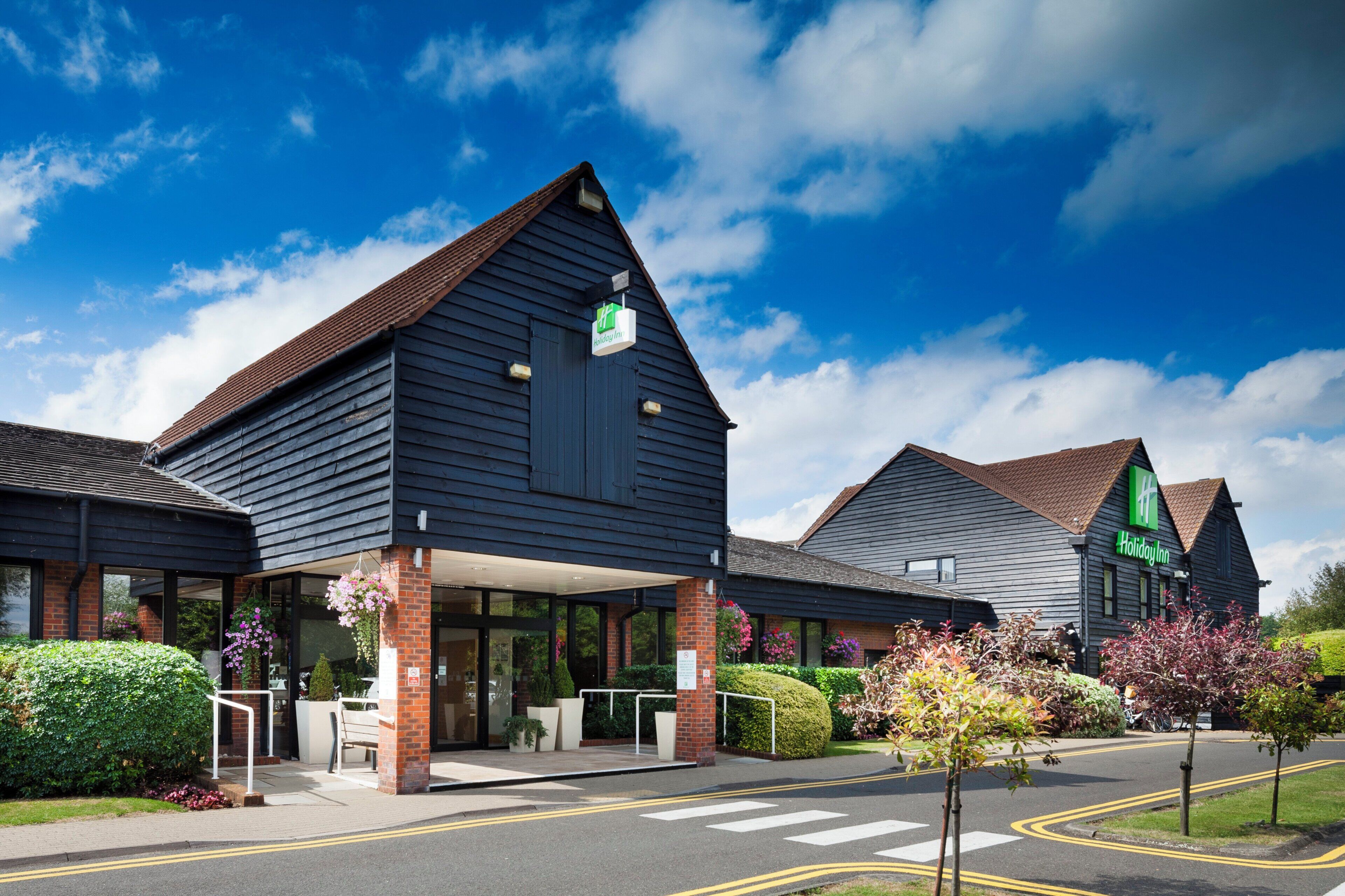 A Holiday Inn with a modern design, featuring a large entrance with a covered patio area, and a clear view of the surrounding greenery.