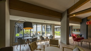 A spacious indoor area with multiple seating arrangements, including round tables and chairs, and large windows providing natural light. - Holiday Inn Cambridge by IHG (Cambridge)