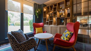 A modern lounge area with a round table, two red armchairs, and a patterned sofa. - Holiday Inn Cambridge by IHG (Cambridge)