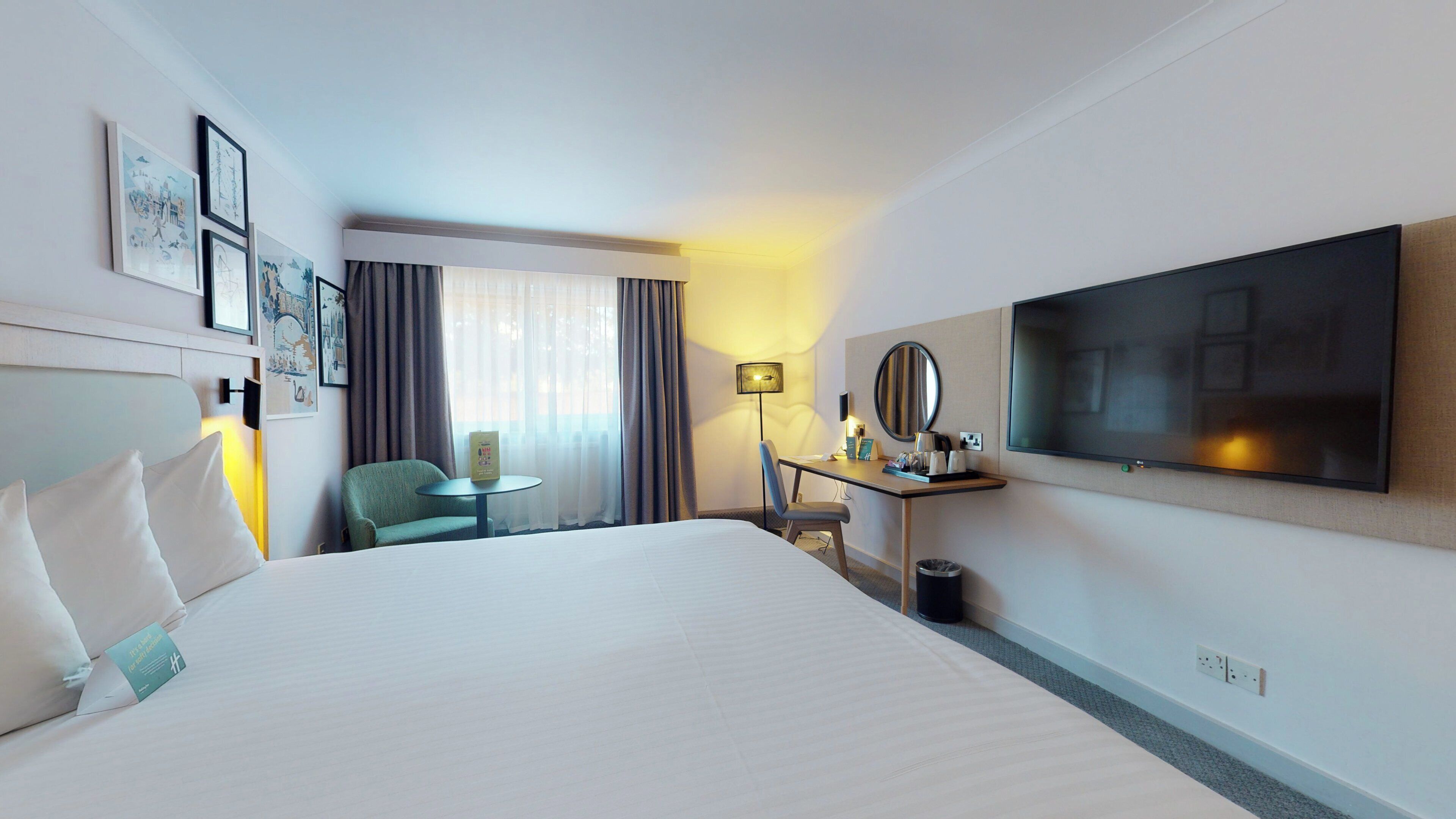A hotel room with a large bed, a desk with a chair, a TV, and a window with curtains.