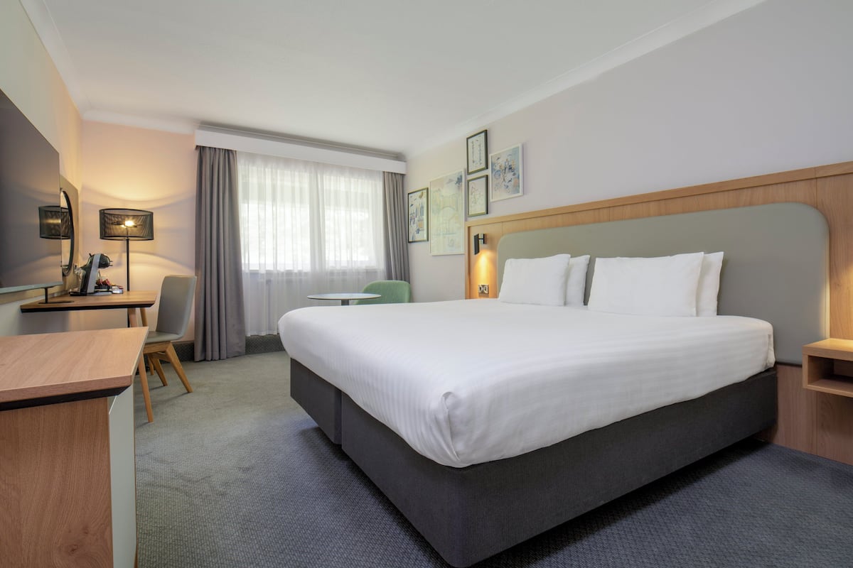 A hotel room with a large bed, a desk, a chair, and a window with curtains.