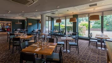 Un restaurante con mesas dispuestas para comer, grandes ventanales que dan a zonas verdes y una alfombra estampada.